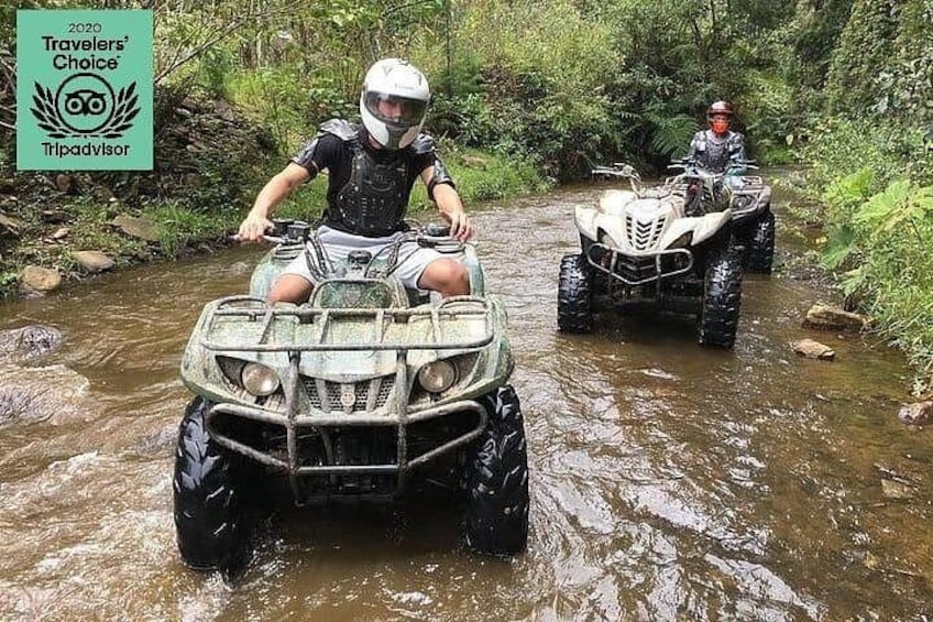 Two off-road vehicles crossing a shallow river in a forested area. 1