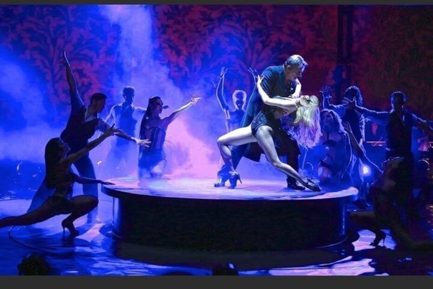 Uno spettacolo dal vivo con ballerini in pose dinamiche, una figura centrale in costume blu e uno sfondo illuminato con luci rosse e blu. 2