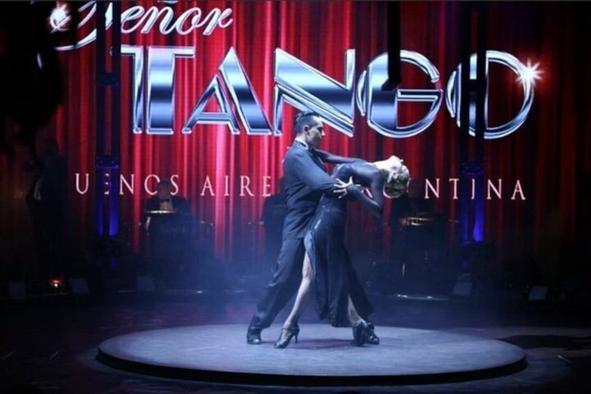 Una coppia che esegue un ballo tango su un palco con uno sfondo a tenda rossa e le scritte 'TANGO' e 'U.NCS AIRENTINA'. 1