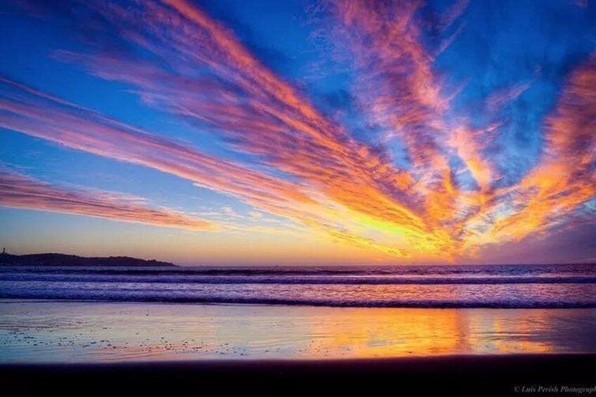 Ein Sonnenuntergang über einem Strand mit leuchtenden Farben am Himmel und ruhigem Wasser, das die Szene spiegelt. 5