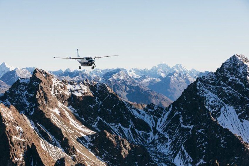 Een klein vliegtuig vliegt boven ruige, met sneeuw bedekte bergen. 4