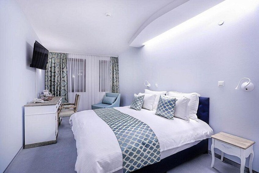 Een moderne hotelkamer met een bed, nachtkastje, bureau, stoel en een aan de muur bevestigde televisie. 5