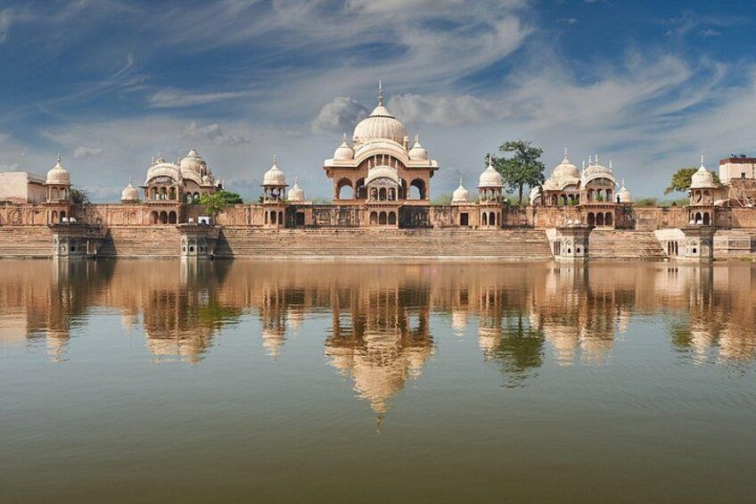 A historic building complex with domed structures and a calm water body in the foreground. 1
