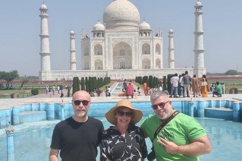 Three people standing in front of the Taj Mahal with a pool in the foreground. 4