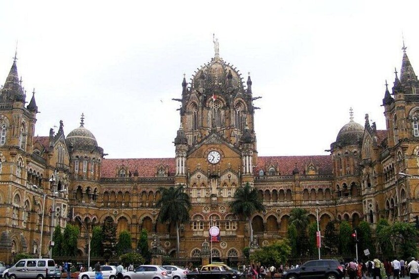 A historic building with a prominent clock tower, arched windows, and a red-tiled roof. 1