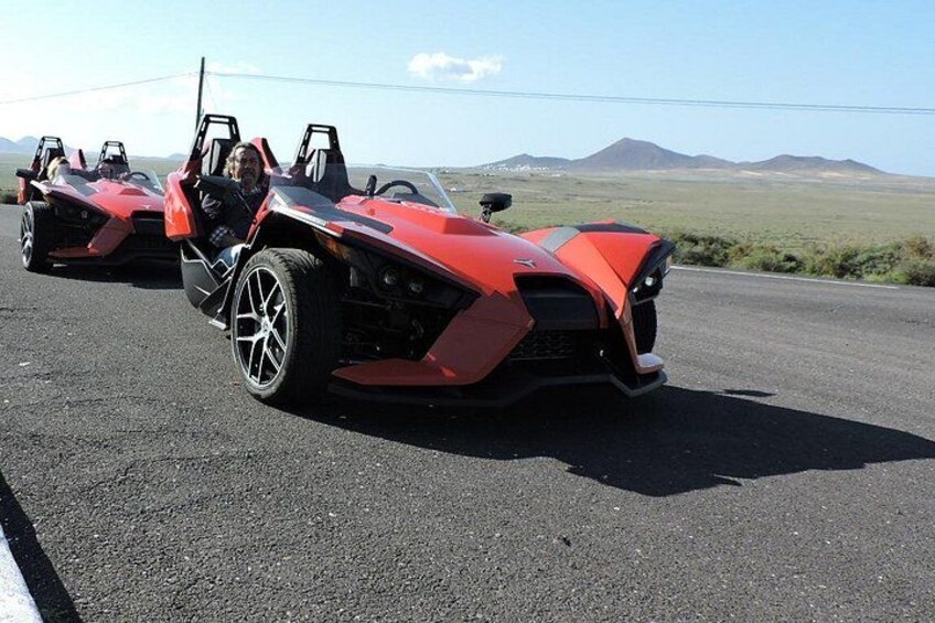 Two red sports cars parked on a road with a mountainous landscape in the background. 1