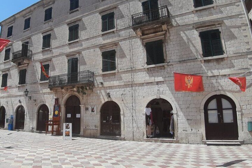 A historic building with arched doorways and a tiled plaza. 1
