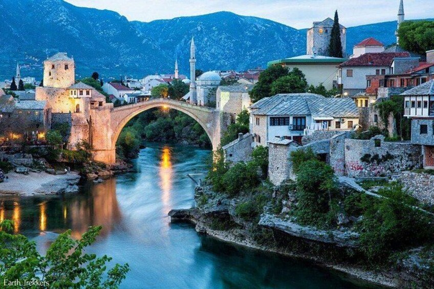 A stone bridge over a river, historic buildings, and a mountain backdrop. 1