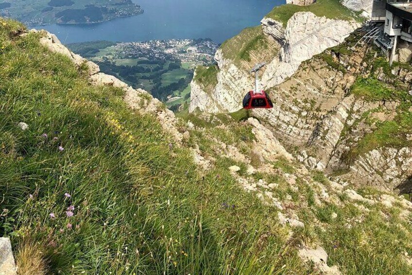A cable car on a mountain with a view of a town and lake below. 1