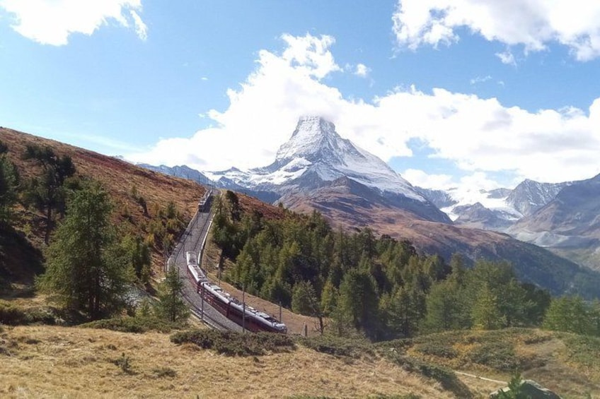 Un train circule sur une voie ferrée de montagne, entouré d’arbres et de sommets enneigés. 2