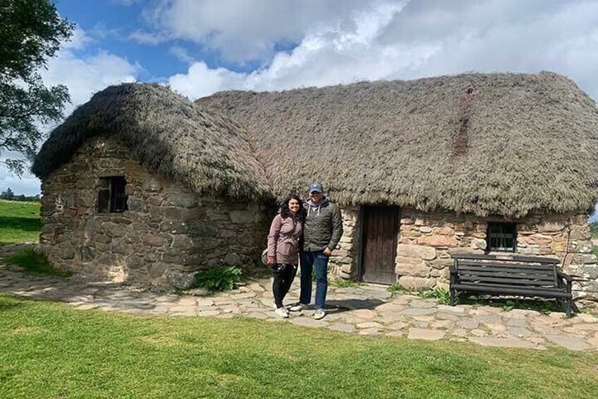 A stone house with a thatched roof, a wooden bench, and a grassy field. 4