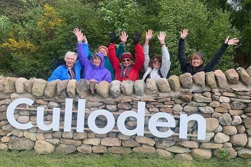 A group of people standing in front of a stone wall with the word 'Culloden' written on it. 5