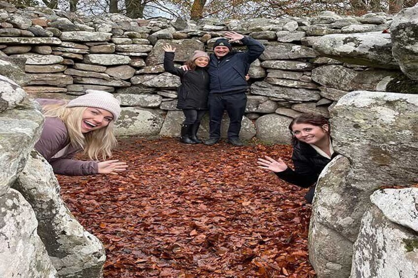 Three people posing in front of a stone wall with a pile of red leaves on the ground. 5