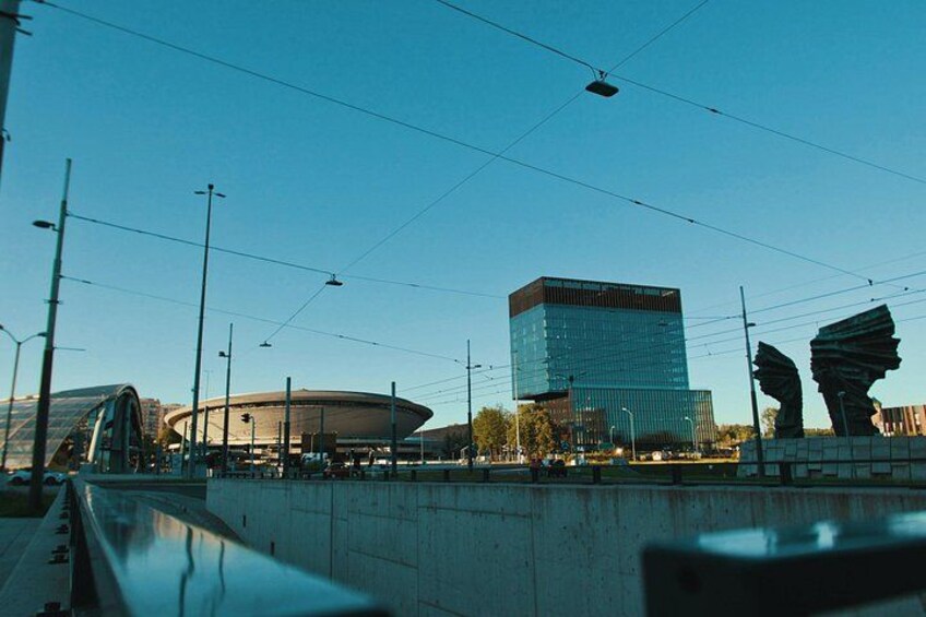 Un paisaje urbano moderno con un estadio grande, un edificio distintivo con techo curvo y un rascacielos alto. 3