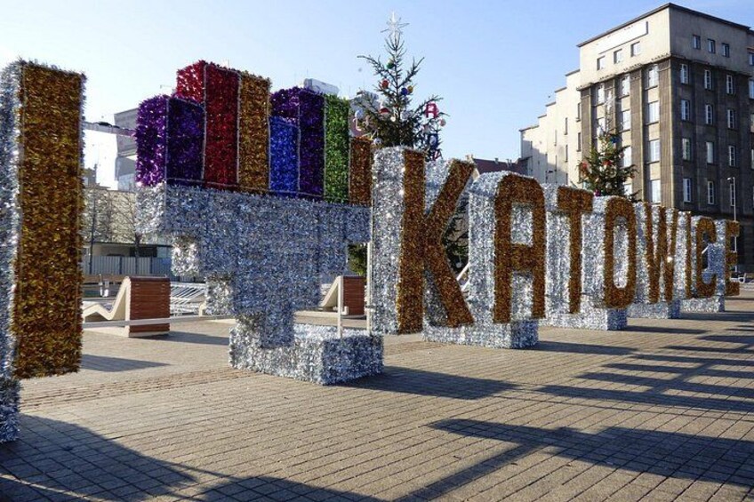 Una decoración llamativa con la palabra 'KATOWICE' en letras grandes, rodeada de guirnaldas de colores y pequeños árboles. 4