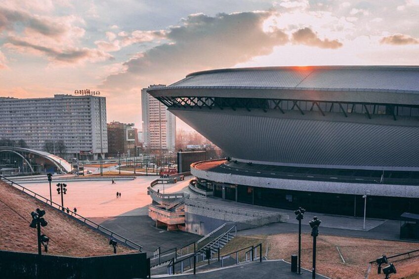 Un estadio con una estructura de techo singular, rodeado de edificios urbanos y un paisaje montañoso. 5