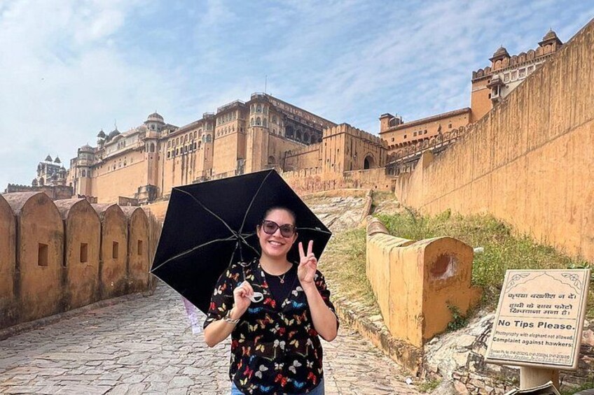 Une personne tenant un parapluie devant un fort historique, sur lequel est affiché un panneau indiquant : « Merci de ne pas laisser de pourboire. » 4