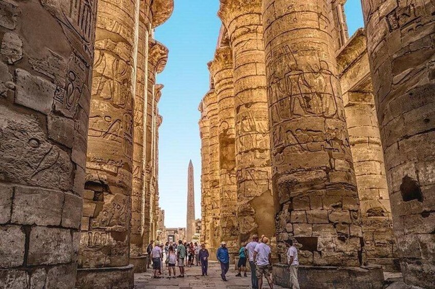 Ancient stone columns with carvings, a clear sky, and tourists walking through. 2