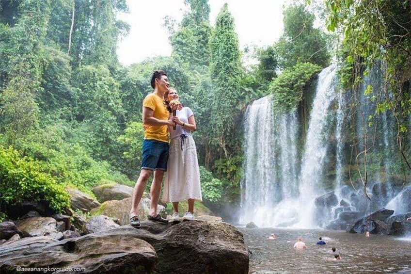 A waterfall, lush greenery, and people standing on rocks. 3