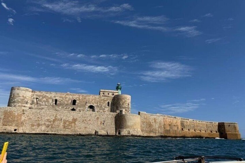 A fortified structure with a tower and a statue, overlooking a body of water. 4