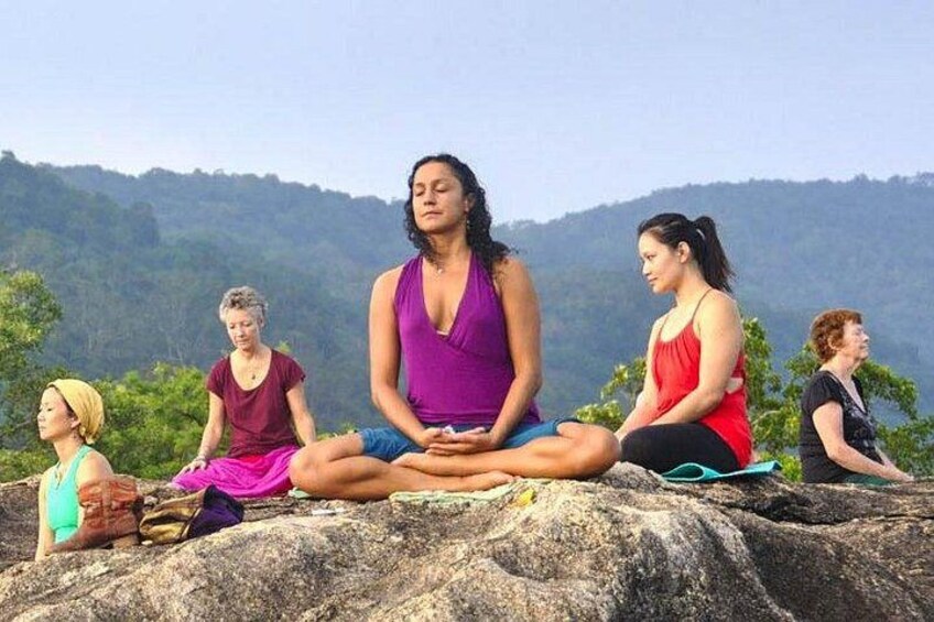 A group of people meditating on a rock formation with a mountainous landscape in the background. 2