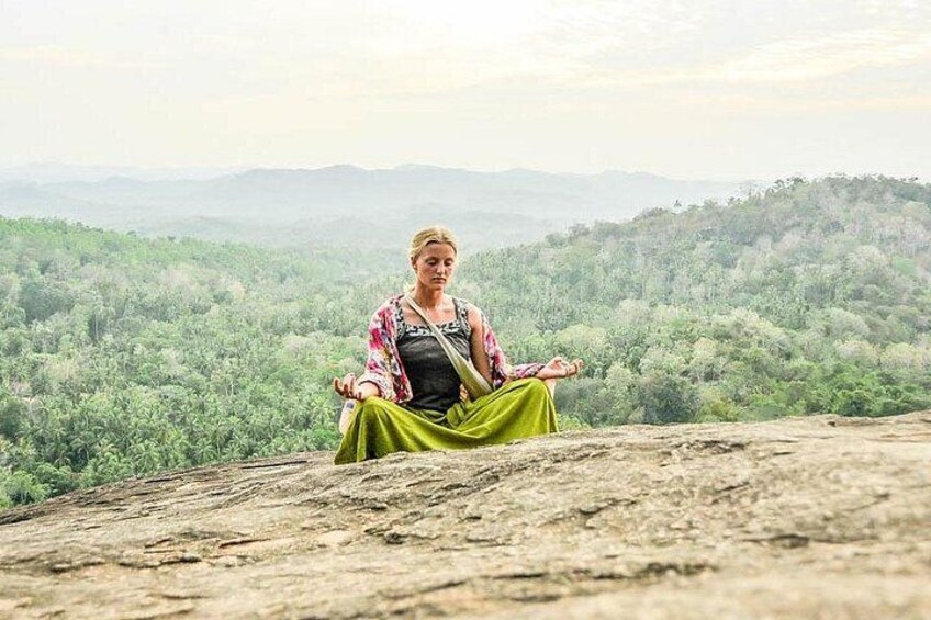 A person sitting cross-legged on a rocky outcrop with a mountainous landscape in the background. 5