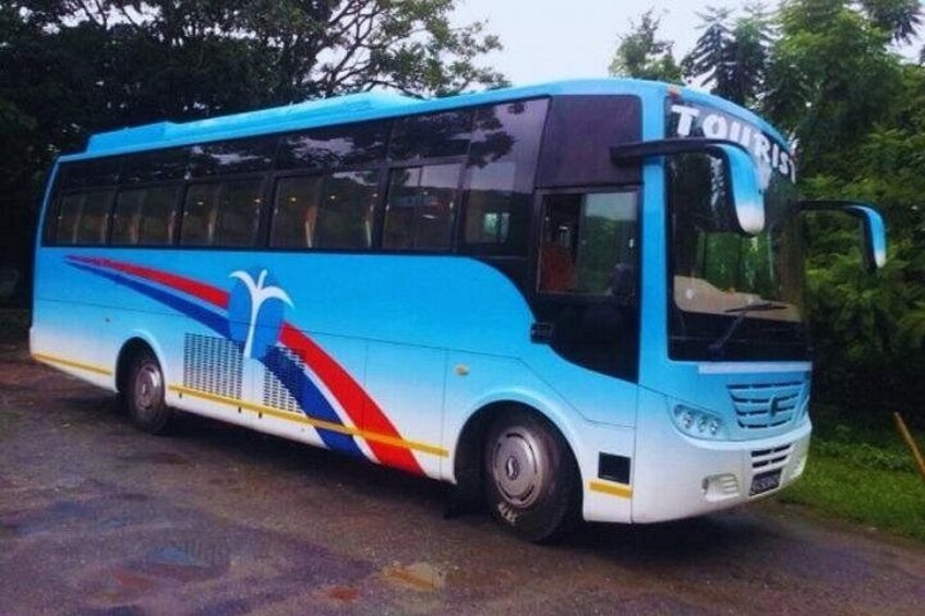 A blue and white bus with 'TOURIST' written on the front, parked on a road with greenery in the background. 3