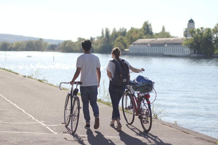 Two people walking along a riverside path with bicycles. 2