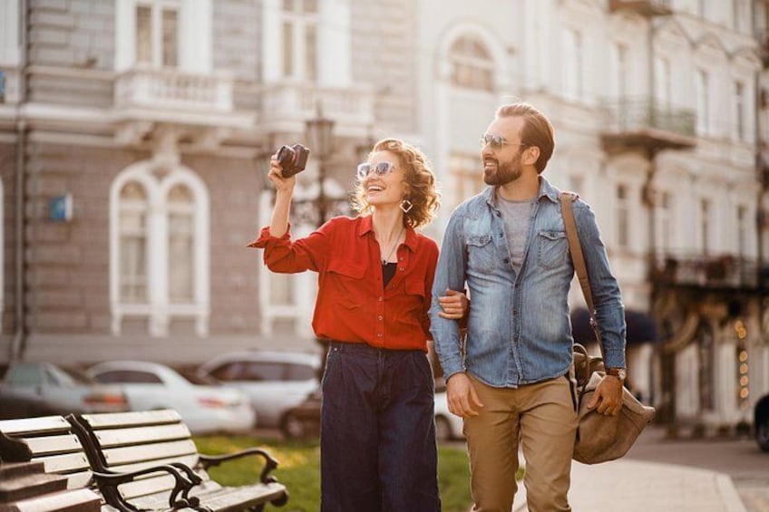 Two people walking on a sidewalk, one holding a camera. 5
