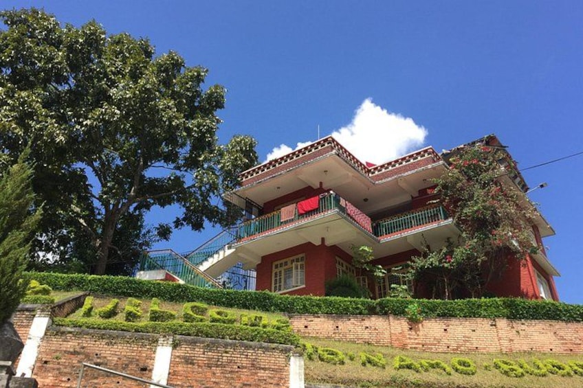 A red building with a balcony, surrounded by greenery and a large tree. 2