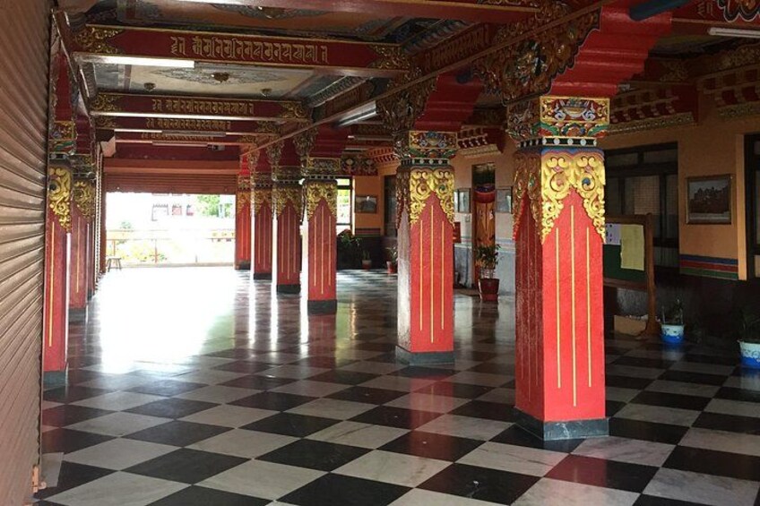 A corridor with checkered flooring, red pillars with gold accents, and traditional architectural details. 1