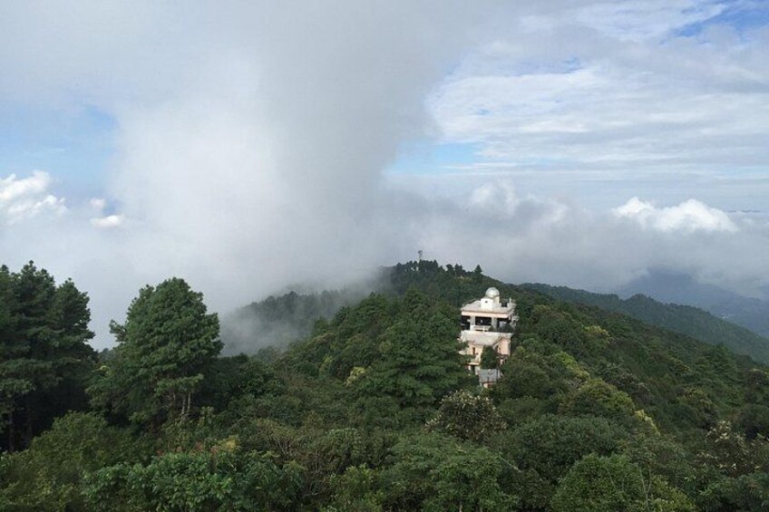 A white building on a hill surrounded by dense green forest and mist. 3