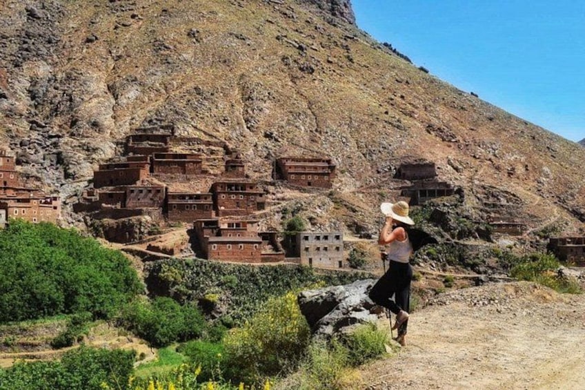 Une personne portant un chapeau, debout devant un paysage montagneux parsemé de bâtiments en terrasses. 1