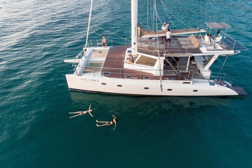 Eine weiße Yacht namens „SAE LANKA“ mit Personen auf dem Deck und zwei Personen, die im Wasser schwimmen. 5
