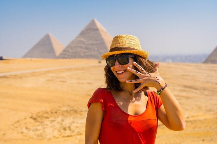 Une personne portant un haut rouge et un chapeau de paille, devant les pyramides. 1