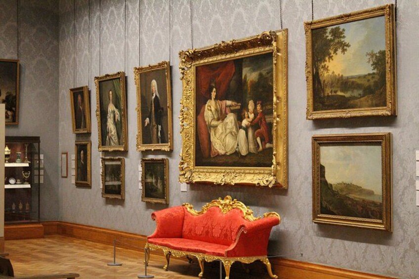 Una galería con pinturas enmarcadas en la pared y un sofá de terciopelo rojo al frente. 5