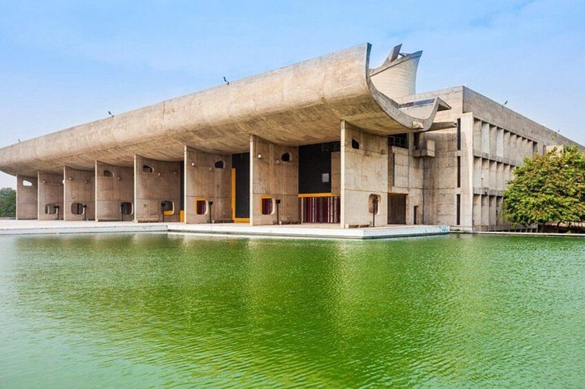 A large concrete building with a unique architectural design, a reflective water body in front, and a clear sky. 2