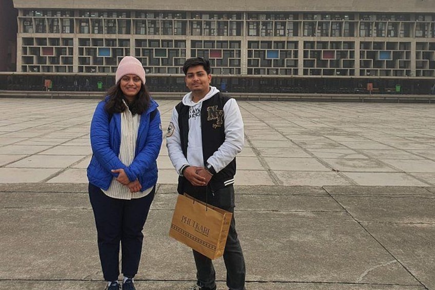 Two people standing in an open plaza with a large building in the background. 5