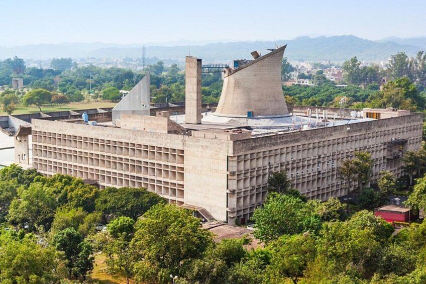 A large industrial building with a unique conical roof, surrounded by lush greenery and distant mountains. 3
