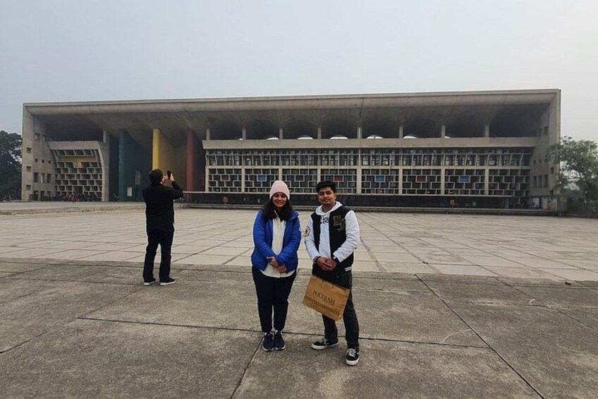 A large, modern building with a unique architectural design, a person taking a photo, and another person holding a bag. 4