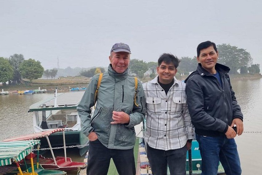 Three people standing by a boat on a misty lake with trees in the background. 1