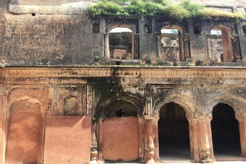 An ancient structure with arched doorways and a balcony with vegetation. 5