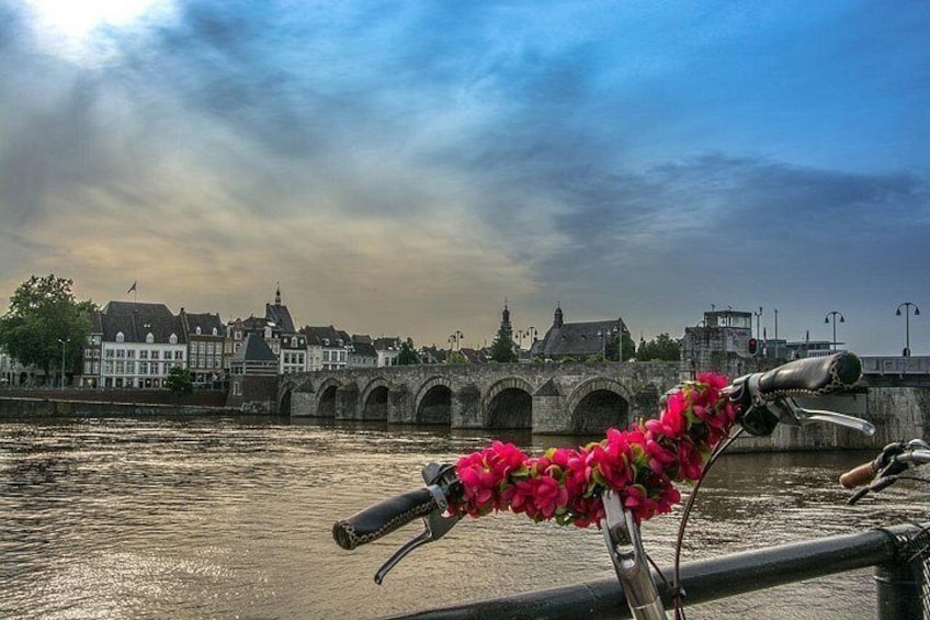 A river with a bridge, a bicycle with pink flowers, and buildings in the background. 5