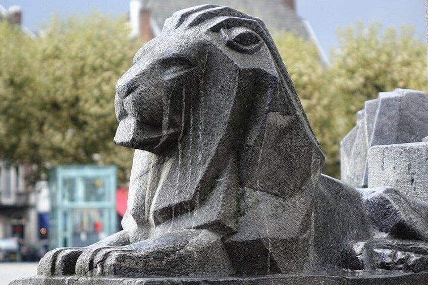 A stone sphinx statue with a lion's head, set against a backdrop of trees and buildings. 3