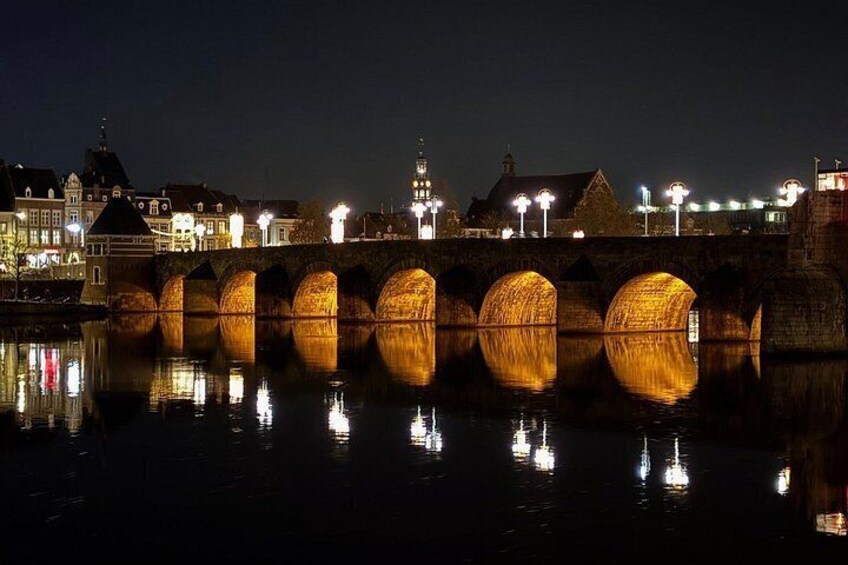 A stone bridge with illuminated arches reflecting on the water at night. 3