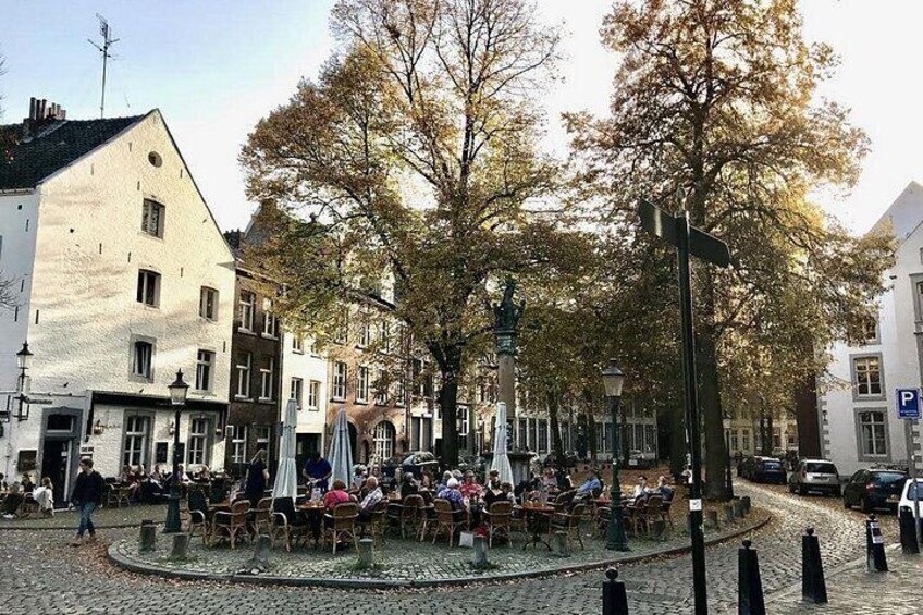 A cobblestone square with outdoor seating, trees, and historic buildings. 2