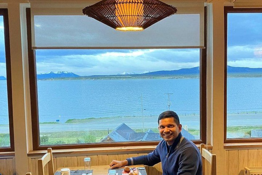 A person seated at a table with a view of a large body of water and distant mountains. 4