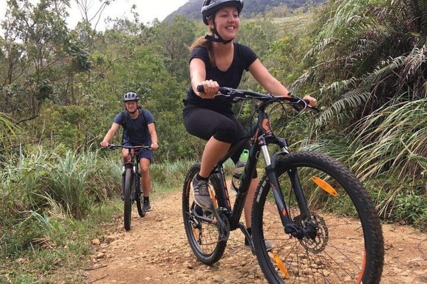 Two cyclists on a dirt path surrounded by greenery. 3
