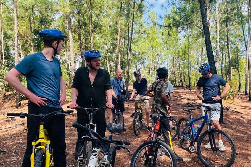 Un groupe de cyclistes se trouve dans une zone boisée, parsemée d’arbres et de sentiers de terre. 2
