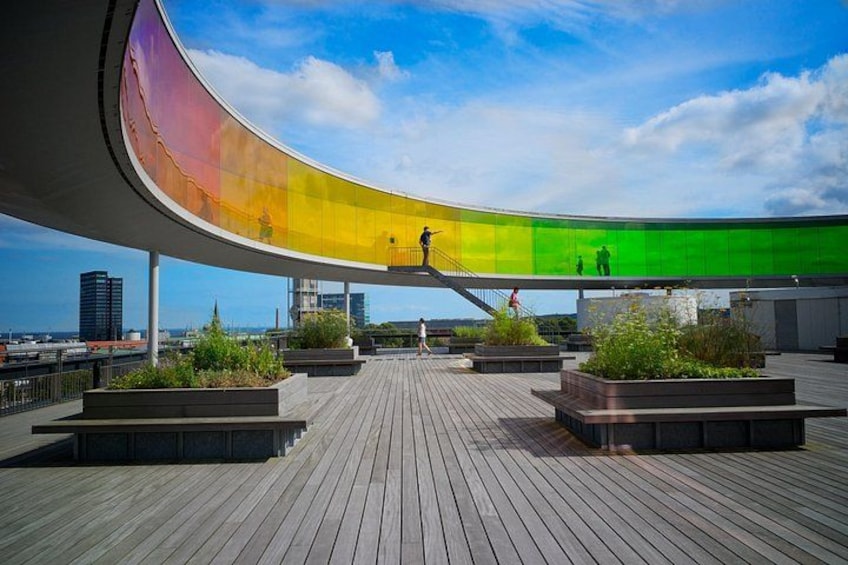 A curved glass structure on a rooftop with wooden flooring and planters. 2